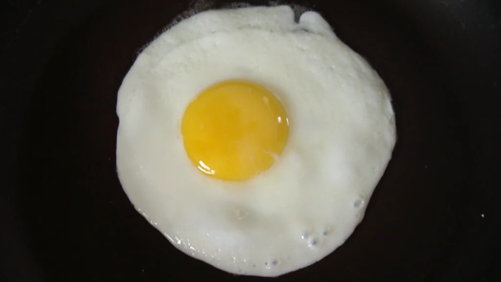 A single, sunny-side up fried egg with a perfectly round yolk, cooking in a black cast-iron skillet.